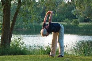 Older man performs yoga by tranquil lake